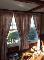 Floral patterned drapes covering a window, tied back, with sunlight streaming in.