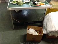 Wide angle view showing the Pro-Action ping pong table with various items on top and a cardboard box with golf balls below.