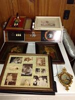 Photo shows 8 framed art pieces and vintage photos arranged on a vintage stereo console against a wood-paneled wall. Items include a small dressed figure in Scottish attire, framed photographs and paintings with Victorian and Scottish themes.