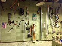 Overview of various tools including wrenches, paint brushes, screwdrivers, scythes, and hardware on a green pegboard wall.