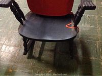 Close-up view of the dark stained wooden rocking chair showing contoured seat and turned armrest and legs
