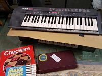Yamaha Portatone electronic keyboard with 44 keys on top of its box, alongside Scrabble and Checkers board games in boxes and Yamaha music instructions.