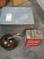 Photo of the milk box, brown jug, and red gasoline can placed together on the floor showing the items.