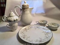 Noritake fine china set displayed showing coffee pot, individual teapot, cups, and dinner plate with floral patterns and gold trim.