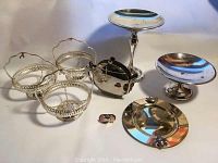 Photo showing entire lot of silver plated serving pieces including pedestal dishes, teapot shaped napkin holder, serving plate, place card holder, and three round servers.