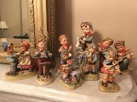 Group photo of 10 hand-painted figurines resembling Hummel style, arranged on a mantelpiece showing varying poses and activities of children, to illustrate overall lot condition and quantity.