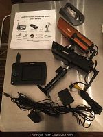 Uniden surveillance system components laid out: two cameras, portable receiver, multiple power adapters, cables, and user manual.