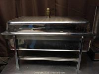 Front view of the chafing dish with lid on, showing the knob handle on top and sturdy frame.
