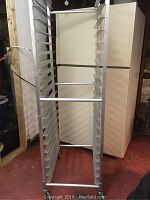 Front and side views of an aluminum commercial bakery rolling rack with 20 evenly spaced slots, set on four caster wheels, approximately 21x27x69 inches.