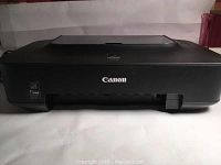 Front view of black Canon iP2702 printer showing Canon logo and front paper output slot.