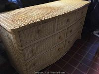 Front and partial top view of wicker dresser showing woven wicker material and curved front.