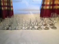 Various clear glasses of different styles arranged in a row on a white surface with a plaid curtain background.