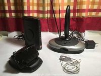 Zoom wireless modem, Radio Shack indoor TV antenna, handsfree cellphone holder, travel charger on table with curtain background