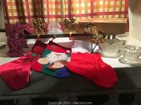 Photo showing three red Christmas stockings with various decorations, three gold bow stocking hangers, a white Lenox candle holder, and a cut glass candle holder on a table.