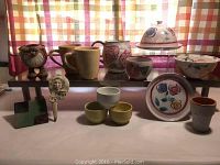 Front photo displaying all pottery items on table with light plaid curtain background, shows variety of sizes and styles, floral and abstract painted designs.