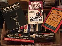 Photo showing various books including 'Pumping Iron', 'Awaken The Giant Within' and 'The Healing Power of Mind' on top of several cassette boxes.