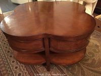 Top and side view of brown cloverleaf-shaped wood coffee table showing drawers and lower shelf.