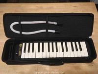 Closed black carrying case with flexible mouthpiece tube secured inside lid and Hohner Student 32 melodica keyboard inside bottom compartment.