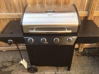 Photo of the Thermos gas grill showing front view with three control knobs, side burner, and temperature gauge on lid.