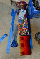 Lot showing Milliflori multicolored floral pattern vase, blue tapered glass vase, and orange three-pocketed candle holder on carpet.