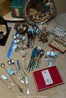 Photo showing assortment of serving spoons, forks, pie server, boxed souvenir forks and spoons, silverplate bowl and various small utensils.