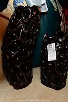 Two carved wood sculptures on a carpeted floor, showing dark finished human figures in intertwined climbing poses.