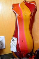 Front view of the colorful glass woman figure sculpture against a wood background and electrical outlet.