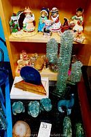 Full view of shelf displaying figurines, geode pieces, glass cactus art, and mineral carvings on black surface.