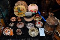 Overview of diverse native and African art pottery and drums grouped on black surface with size tags visible