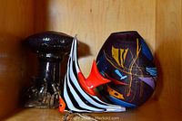 Three hand-blown glass art pieces: a dark mushroom sculpture, a striped fish figurine, and a decorated purple vase.