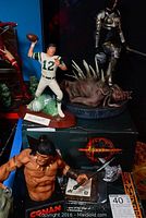 Photo showing Joe Namath football figurine with number 12 jersey, holding a football, signed and on a stand, Conan figure and Hellgate London warrior figure in background
