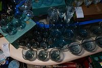 Photo showing multiple clear or aqua-tinted glassware pieces grouped together on a table including glasses with stems and original blue boxes.