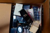 Top view of a box filled with assorted Avon boxed products, mostly dark blue and black packaging with some white boxes and various small items packed tightly
