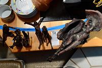 Five metal sculptures of women and one larger clay angel sculpture on wooden surface alongside other kitchenware items.