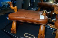 Side view of one camel stool showing leather seat and carved wooden hoof-style legs.