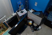 Wide view showing monitor, joystick box, and other electronics packed around a white box on carpeted floor