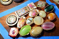 Overview of all 15 cloisonne ring boxes arranged on a wooden surface with floral, scenic, and solid color designs.