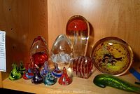 Front view showing nine small swirl-patterned glass kisses, two egg shapes, cube, jellyfish paperweight and green knife