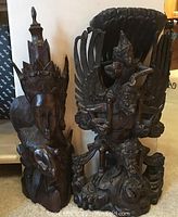 Photo showing both Indonesian carved wood statues standing side by side on floor, highlighting their size and overall structure.