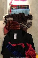 Lot of graduation robe, cap, wool shrugs, poncho, and mink fur stoles arranged on floor.