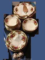 Set of various plates, bowls, serving platter, cake knife, and salt and pepper shakers, all decorated with Old Country Roses floral design and gold trim, neatly stacked and displayed.