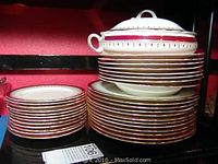Stack of Aynsley bone china dinner plates, soup bowls, side dishes, and a covered serving bowl showing red and gold border design