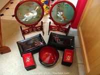 Overall shot of two framed round silk embroidery artworks featuring cat designs, 8 black rectangular dishes and 8 red small rectangular dishes arranged around a large red bowl.