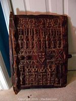 Full view of the carved wood African door standing against a door.