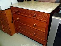 Full view of the wooden dresser with marble top attached, showing the wood grain, three drawers with round knobs.