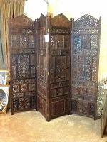 Full view of the four-panel carved teak wood privacy screen standing unfolded in a room.
