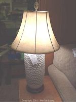 Full view of the lit table lamp showing white fabric shade and perforated ceramic ginger jar base with wooden bottom.