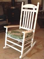 Full view of wooden white rocking chair with vertical slat back and green leaf cushion.