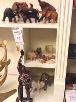 Shelf display of various elephant figurines including wooden, ceramic and stone, and stone turtles