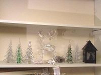 Shelf with six clear glass evergreen trees and a Lucite reindeer figurine with antlers